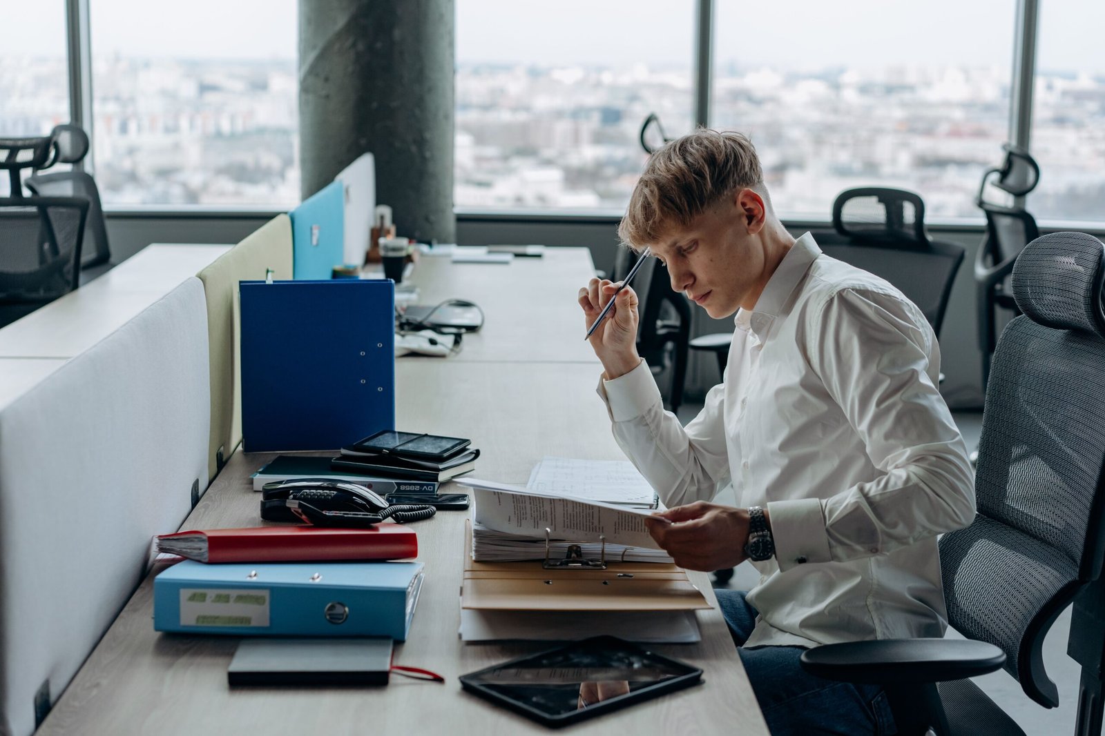 Person an einem Büroschreibtisch mit Aktenordnern, Unterlagen und einem Tablet.